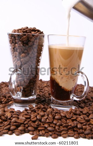 Making of caffe latte:glass of coffee with milk being poured into it, with a glass of beans surrounded by coffee beans