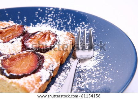 Piece of Plum Pie covered with powder sugar on a blue plate