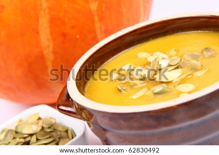 Pumpkin soup decorated with pumpkin seeds and a bowl of seeds and a pumpkin in the background