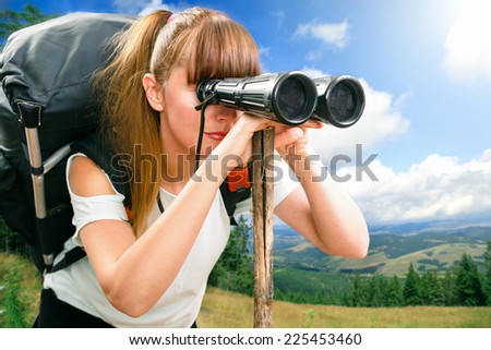 young beautiful woman hiker looking through binocular on mountain in summer