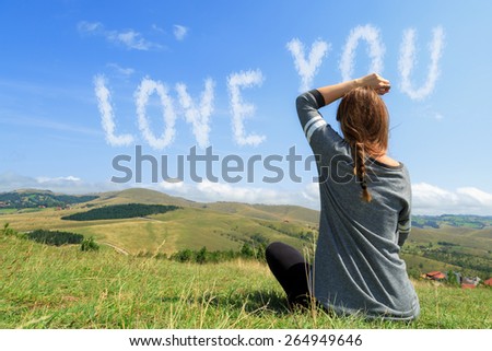 Young woman sitting on top of hill and watching in the message in sky