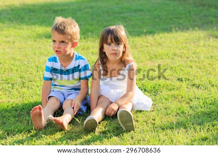 Little boy and a girl sitting on the grass being bored