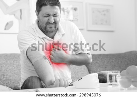Man measuring his blood pressure and having chest pain. Black and white with red highlight of chest.