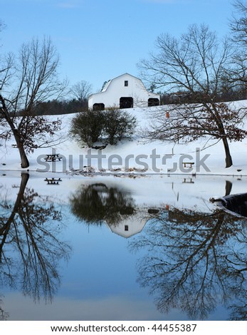 A barn on a hill during the winter. In front of a small pond.
