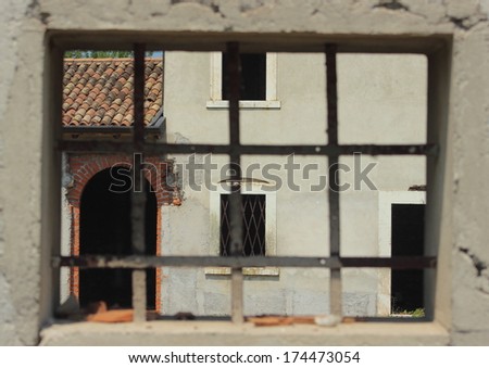 Window with metal bars framing a abandon farm house