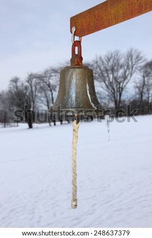 Metal Bell with Winter Snowy Fields in Background. The Bell is used on a golf course.
