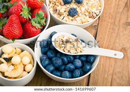 fresh blueberry, strawberry and corn flakes in white porcelain bowl, wooden table