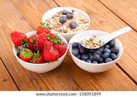 fresh blueberry, strawberry and corn flakes in white porcelain bowl, wooden table