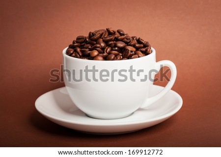 Coffee beans in cup on brown background