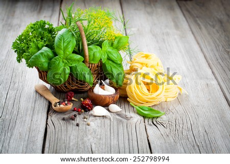 Italian pasta fettuccine nest with wicker basket green herbs, on wooden background