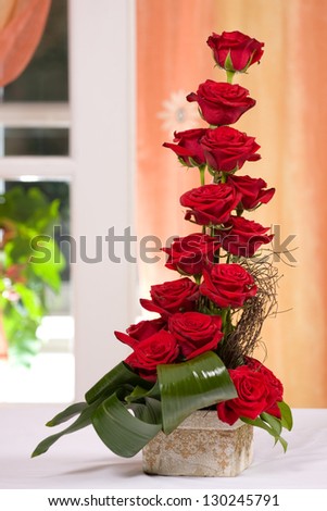 Red roses arrangement on a white table next to a orange curtain
