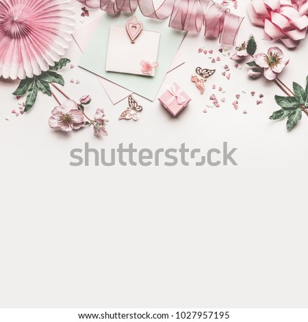 Beautiful pastel pink work space with flowers decoration,ribbon, hearts, bow and card mock up on white desk background, top view, flat lay, border. Wedding invitation or Mother Day greeting concept
