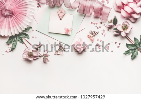 Beautiful pastel pink layout with flowers decoration, ribbon, hearts, bow and card mock up on white desk background, top view, flat lay, border. Wedding invitation or Mother Day greeting concept
