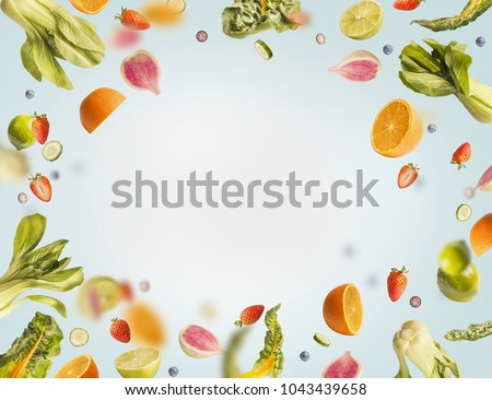 Various flying or falling summer fruits,berries and vegetables on light blue background, frame. Healthy detox food layout concept