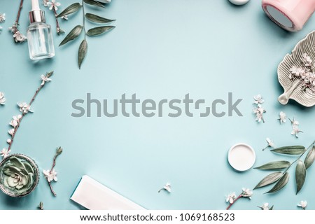 Beauty background with facial cosmetic products, leaves and cherry blossom on pastel blue desktop background. Modern spring skin care layout, top view, flat lay.