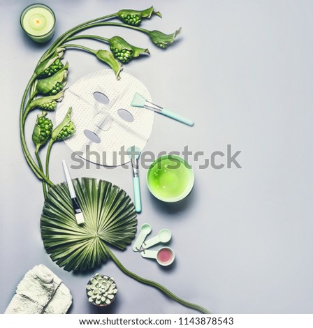 Skin care cosmetic and facial sheet mask. Various serum, cream and gel cosmetics product with tropical leaves and flowers on gray background, top view with copy space. Beauty concept