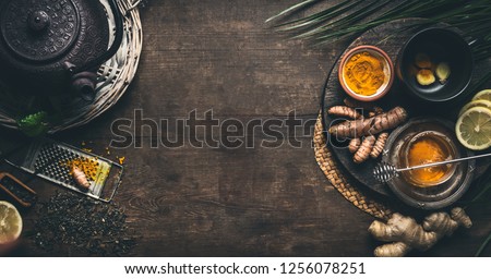 Herbal turmeric tea background. Cup of healthy turmeric spice tea with iron teapot and ingredients:  lemon,  ginger, cinnamon sticks and honey , top view frame with copy space. Immune boosting remedy