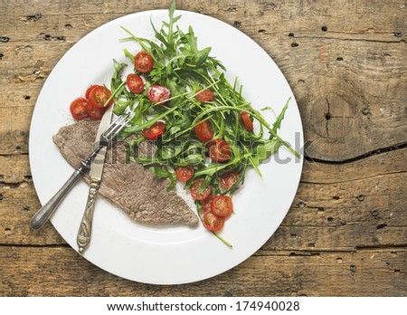 beef with rocket salad and tomatoes on old wood table, dietetic food