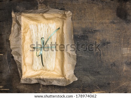 Chinese rice noodles in crumpled paper packaging with green ribbon on an old wooden table
