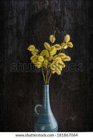 bunch of willow twigs with catkins and yellow pollen,  in old blue vase on dark wooden background