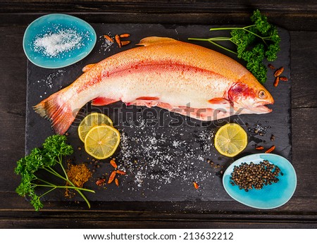 fresh rainbow trout fish with spices on dark wooden table, preparation