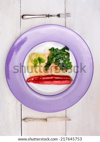 stuffed Red peppers with mashed potatoes and spinach in purple plate , fork and knife on white wooden table, top view