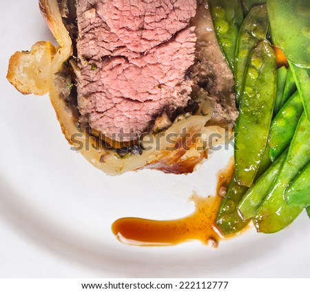 Beef Wellington with green peas on white plate, close up