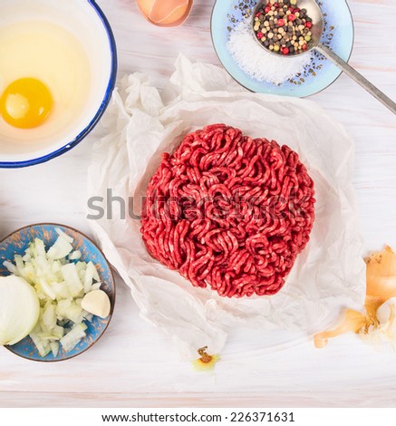 minced meat in paper and Ingredients for meat patties , preparation on white wooden background, top view
