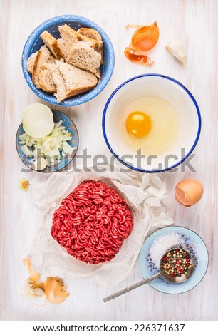 meat patties Ingredients: raw  minced meat , raw egg,chopped onion,garlic,bread,salt and pepper on white wooden background
