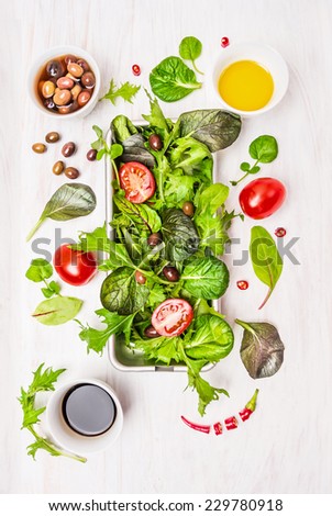 Wild herbs salad with tomatoes,olives,oil and vinegar on white wooden background, top view