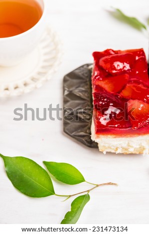 fresh strawberries cake with jelly and cup of tea on white wooden background