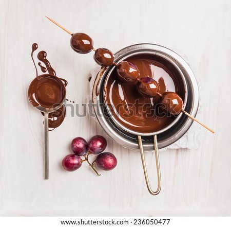 Grapes in chocolate making on white wooden background, top view