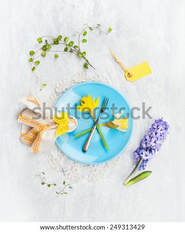 Blue plate with spring flowers, fork, sign and decoration on gray wooden background, top view