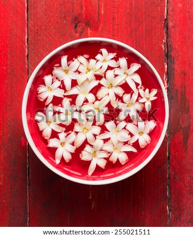White flowers in Bowl with water on red wooden table, SPA background, top view