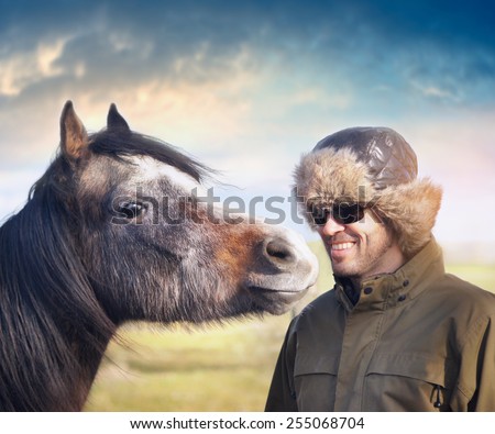 Young horse looking at smiling man in hat ear flaps