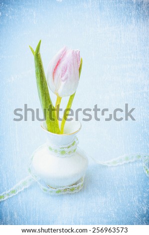 Pink tulip in vase with ribbon on blue textured background, romantic vintage card