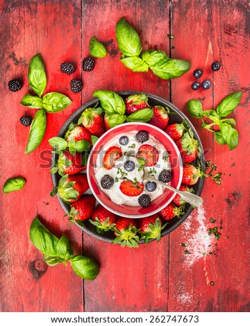 Summer berries blackberries, blueberries, strawberries with cottage cheese, basil leaves and spoon on red wooden background, top view