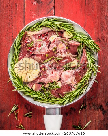Raw meat Double lamb loin chops with rosemary and garlic in white frying pan on red wooden background, top view