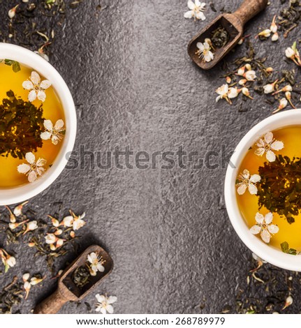 Green Jasmine tea with fresh flowers and tea cups on black stone background, frame, top view, place for text