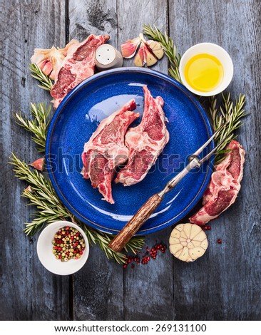 Raw double lamb loin chops with meat fork in blue plate with oil, herb and spices  on  blue wooden background, top view
