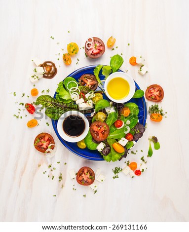 fresh salad with tomatoes,feta cheese, balsamic vinegar and oil in blue plate on white wooden background, top view