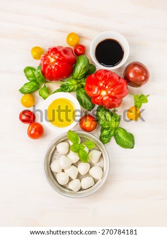 Mozzarella tomatoes salad ingredients with basil leaves,oil and balsamic vinegar, preparation on white wooden background, top view