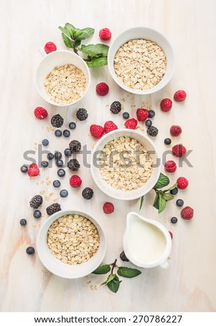 healthy breakfast: oat flakes in bowls, fresh berries and milk on white wooden background, top view
