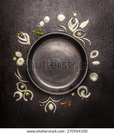 empty black plate with frame of onion slices and spices on dark stone background, top view, copy space