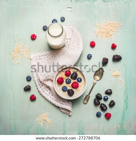 oatmeal porridge, bottle of milk and berries on blue wooden background with kitchen towel, top view
