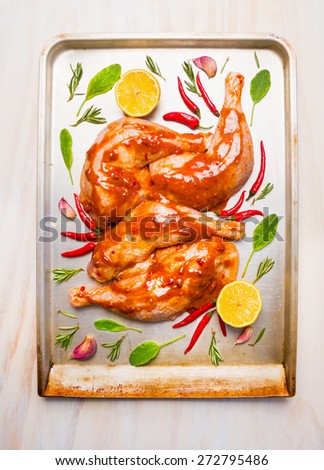 raw chicken legs with red spicy sauce, sage and lemon in bake tray on white wooden background, top view