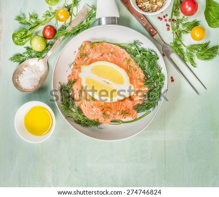 Raw salmon fillet in white Frying pan with oil, fresh seasoning,oil , spoon and fork on green rustic wooden background, top view, place for text