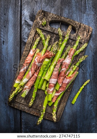 Green asparagus with parma ham on old gutting board, , rustic blue wooden background, top view