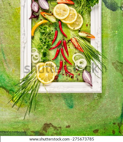 white frame with fresh spices, chili , garden herbs and lemon on green background , top view, place for text