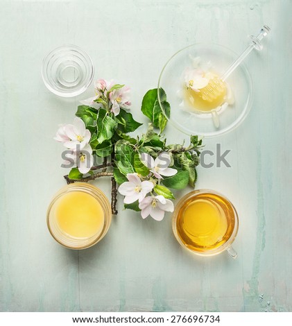 Spring harvest honey in glass jar with dipper, fresh blossom and cup of tea, top view